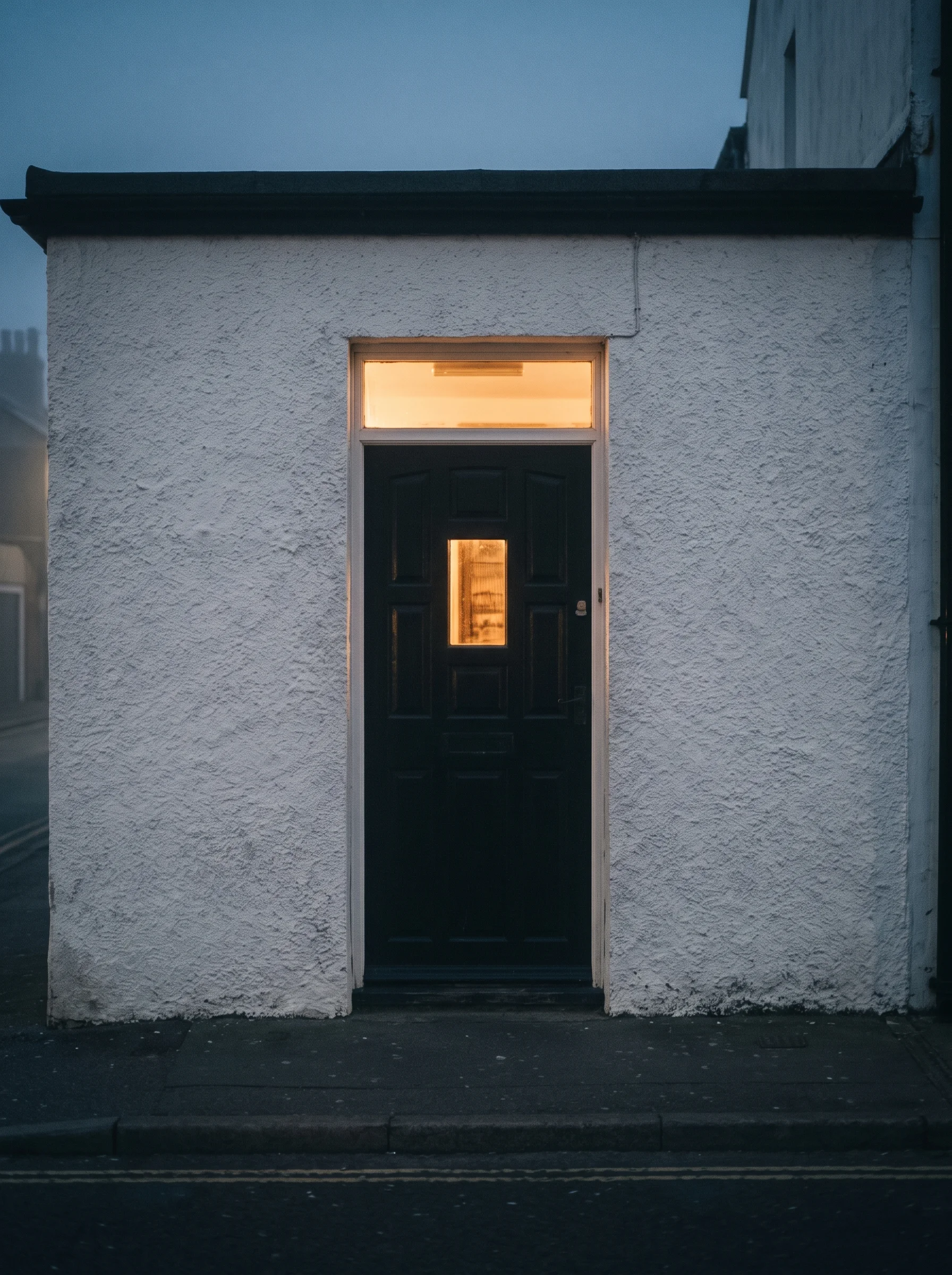 A tar-black timber door in chalk-white render at dusk, one small window lit, sea fret drifting through the lamplight.